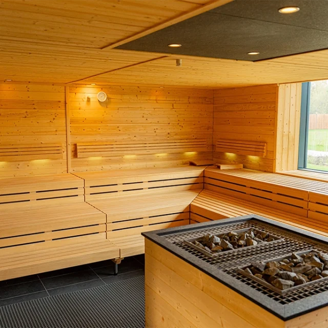Aufgusssauna mit Holzbänken, Saunaofen in der Mitte und Fenster mit Blick in den Aussenbereich